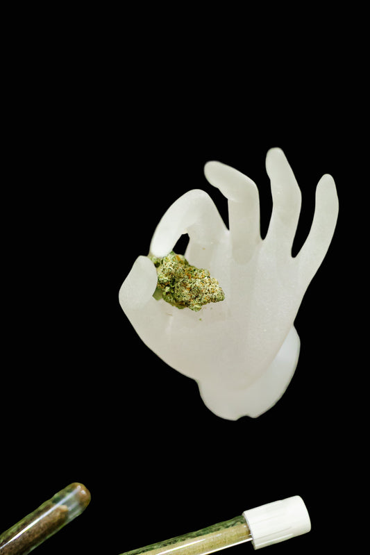 White silicone mold shaped like a hand with cannabis buds on a green surface