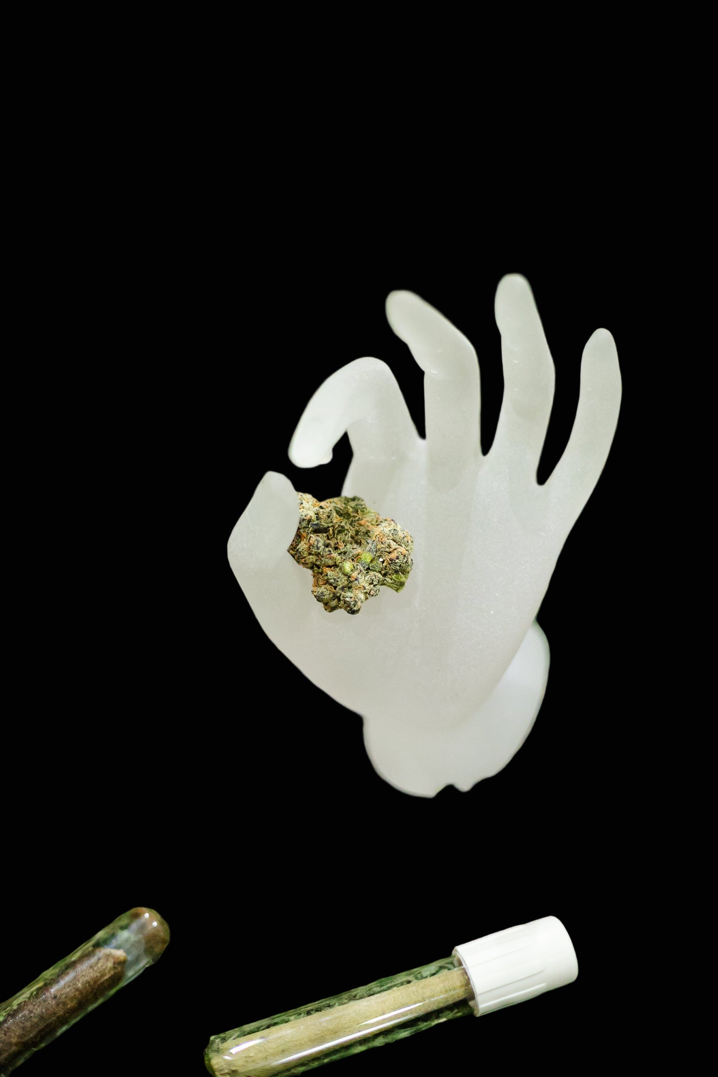 White hand-shaped container with cannabis buds on a green surface with other cannabis products.