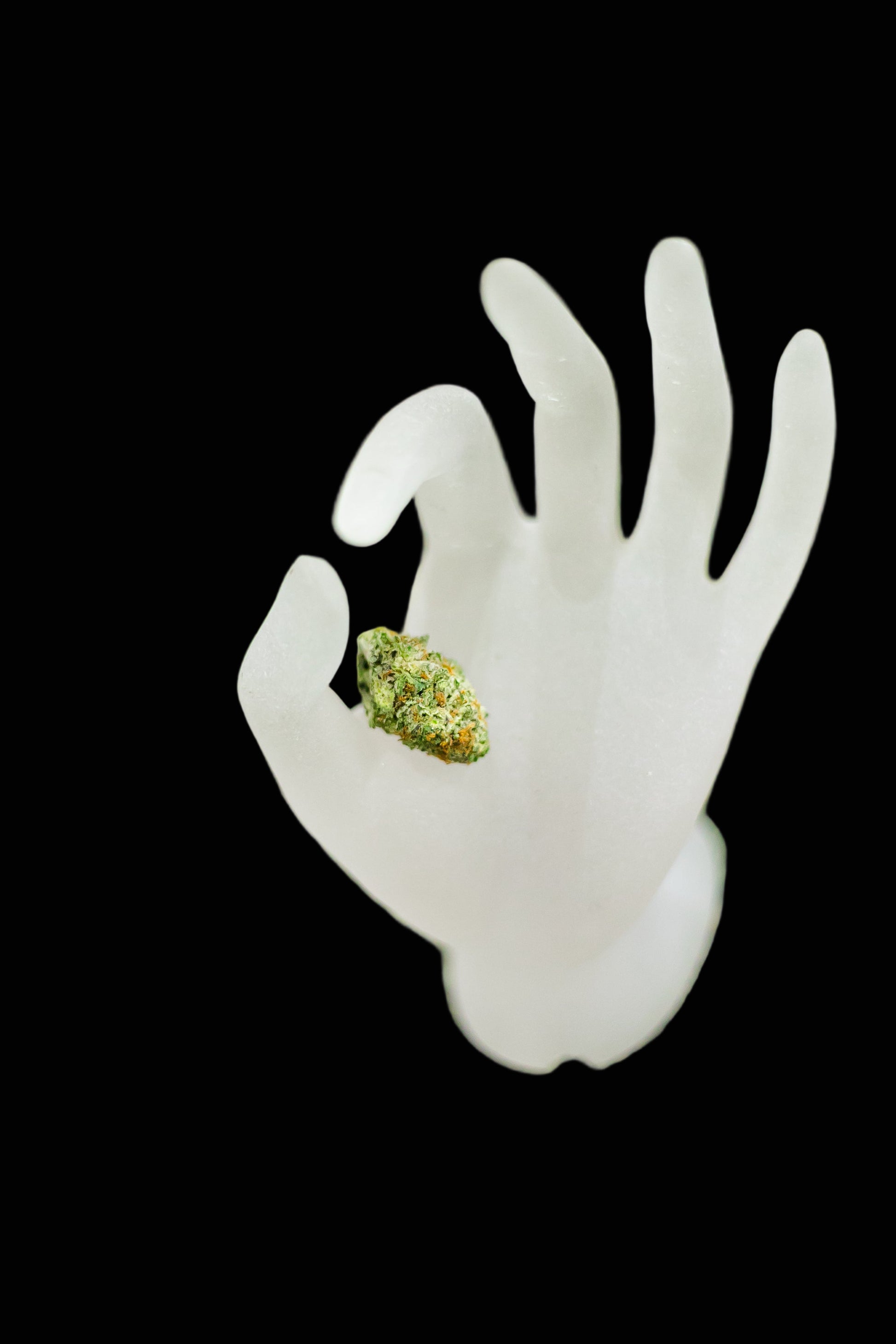 White plastic hand holding a cannabis bud on a green background