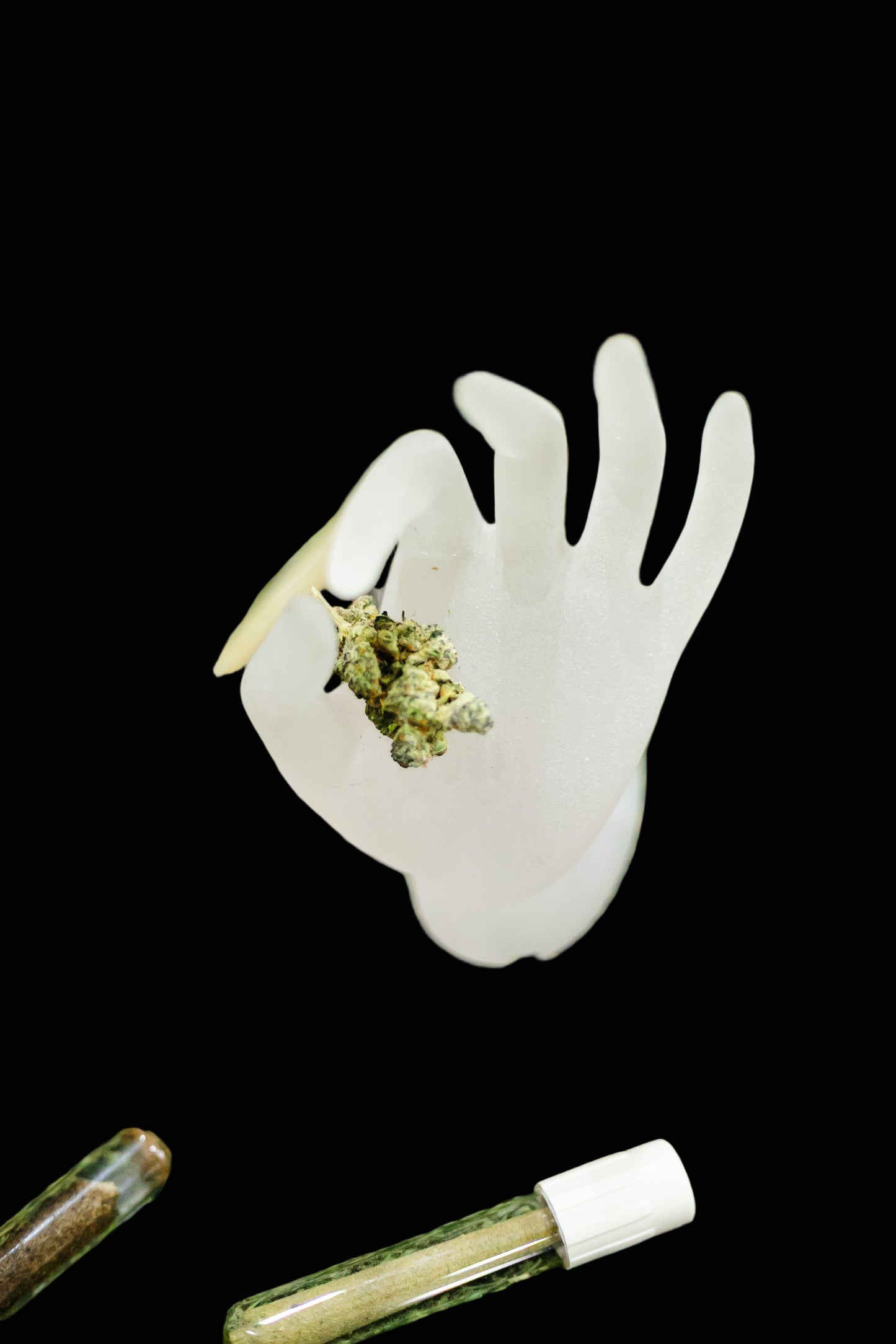 White hand-shaped container with cannabis buds on a grassy surface